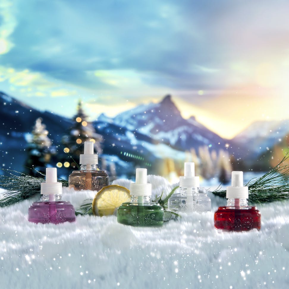 five ScentPlug Refills in snow surounded by slices of lemon, branches, and mountains