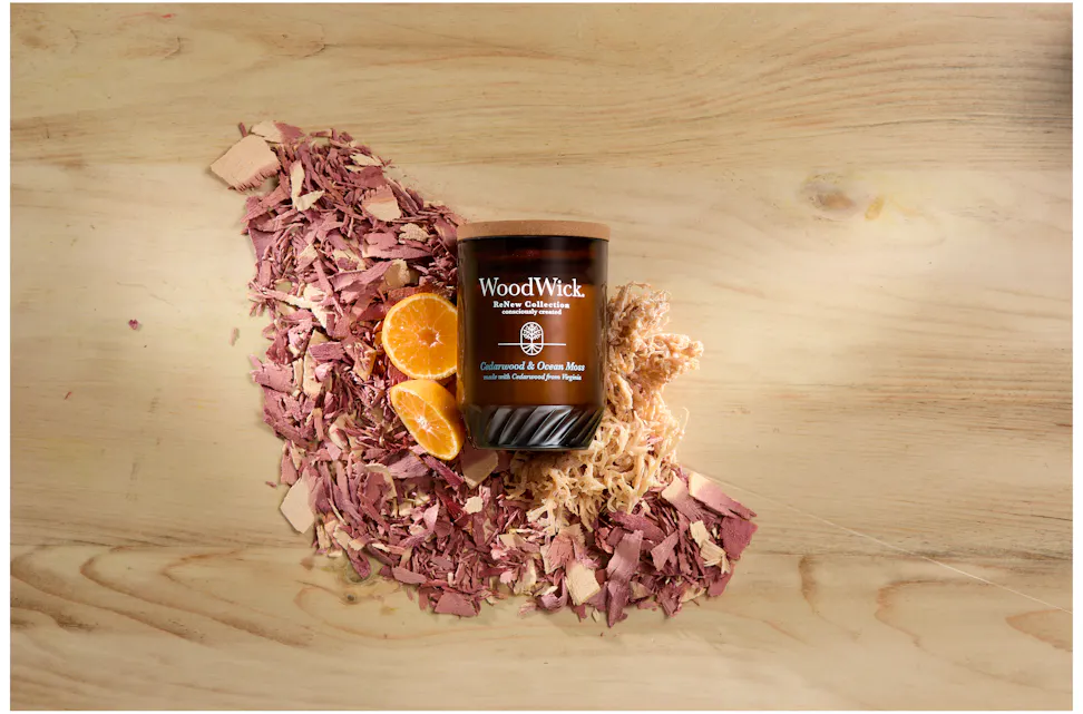 WoodWick ReNew Collection Cedarwood & Ocean Moss Large Candle on a pile of moss, pieces of shaved wood and slices of fruit