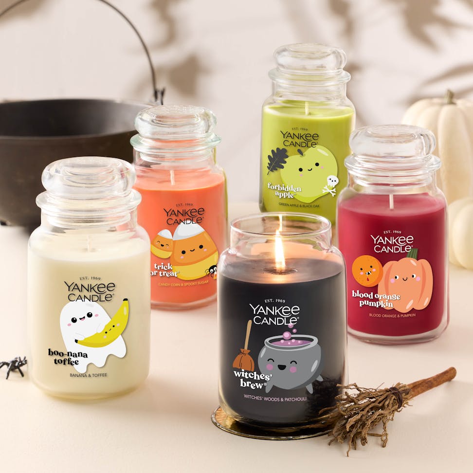 Large black glass candle with bubbling cauldron design, surrounded by festive Halloween-themed jar candles.