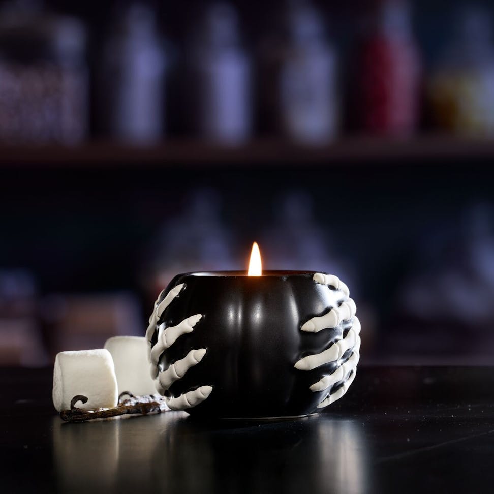 Halloween candle in a black holder with skeleton hands, glowing flame, spooky decor, marshmallows beside it