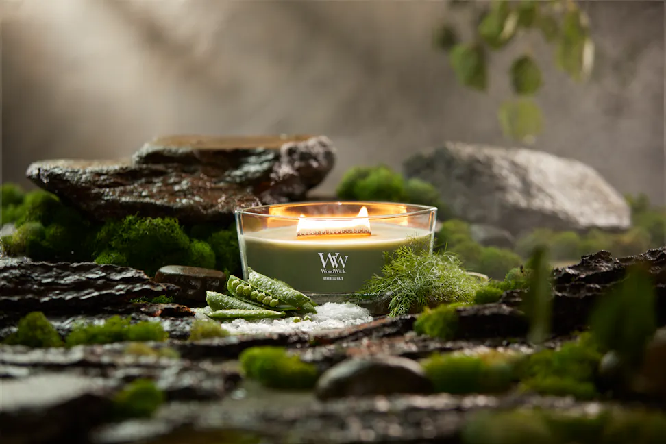 WoodWick Vapour Trails Collection Ethereal Haze Ellipse Candle surrounded by rocks, moss, salt, and snap peas
