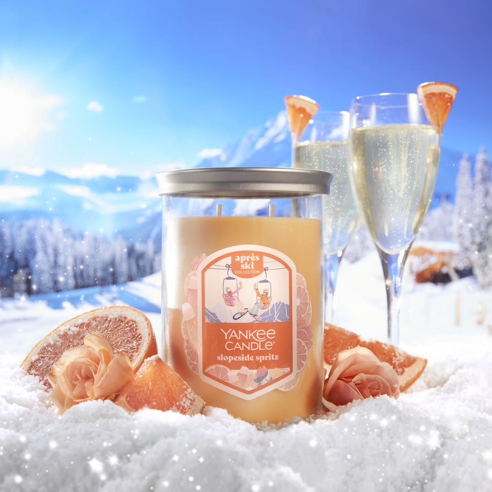 apres ski slopeside spritz tumbler candle on a snowy slope with roses sliced grapefruit and glasses of sparkling wine