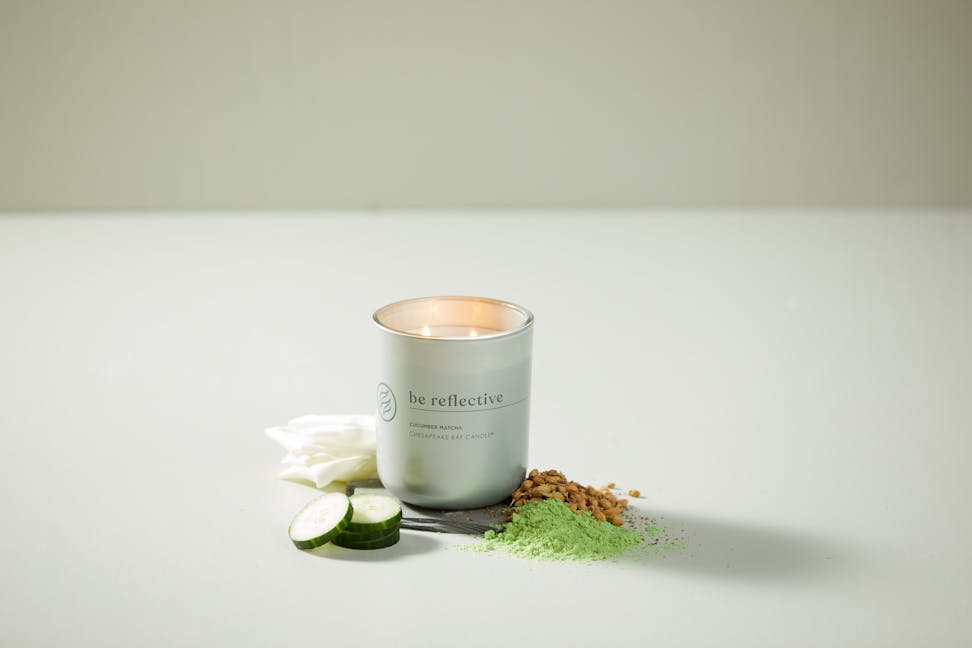 chesapeake bay candle intentions collection be reflective cucumber matcha medium two wick jar candle surrounded by cucumbers, white petals, nuts, and matcha