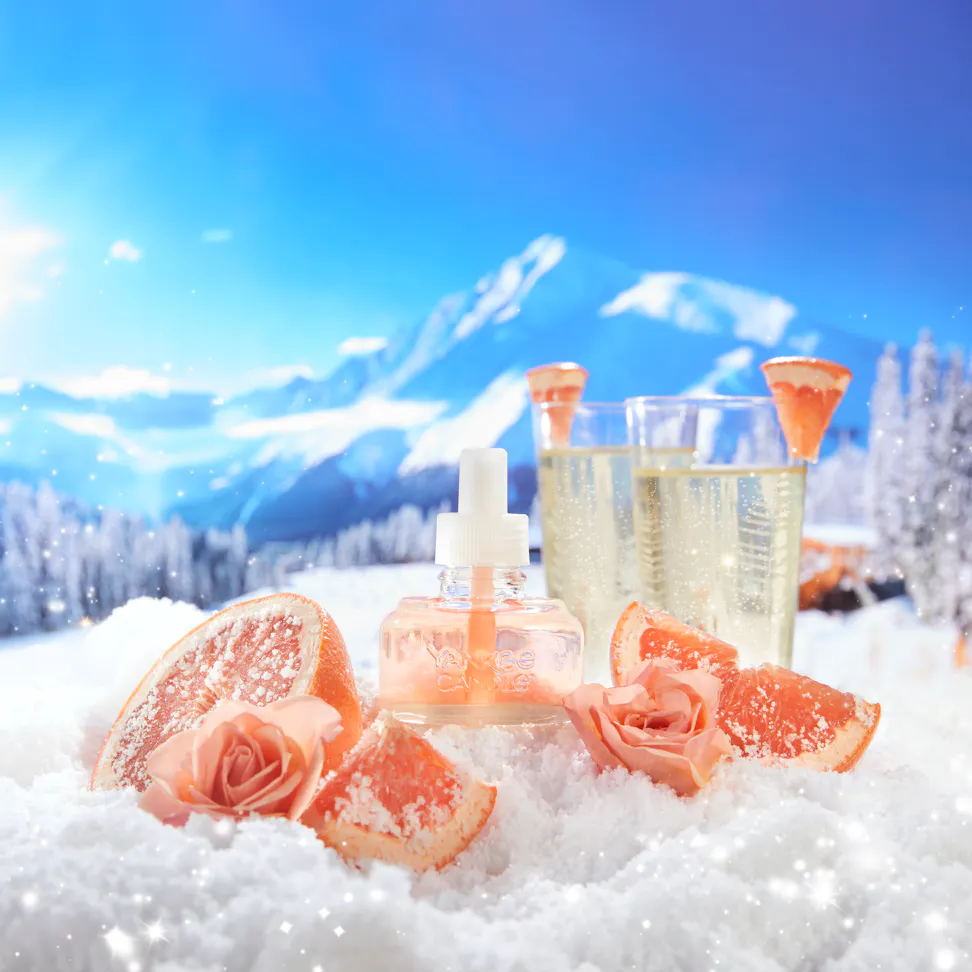 slopeside spritz scentplug refill on a snowy mountainside with sliced grapefruit roses and glasses of sparkling wine