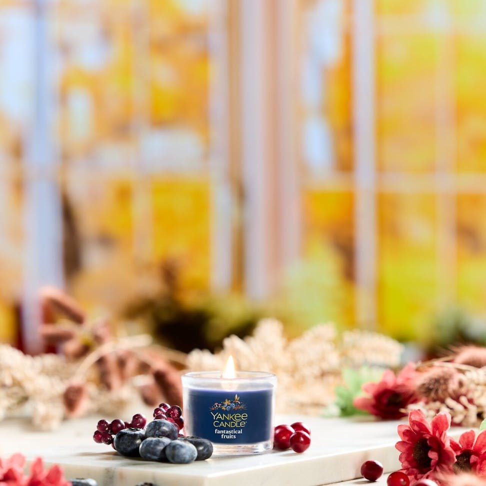 Blueberry scented candle in glass jar surrounded by berries and flowers, cozy autumn home decor scene
