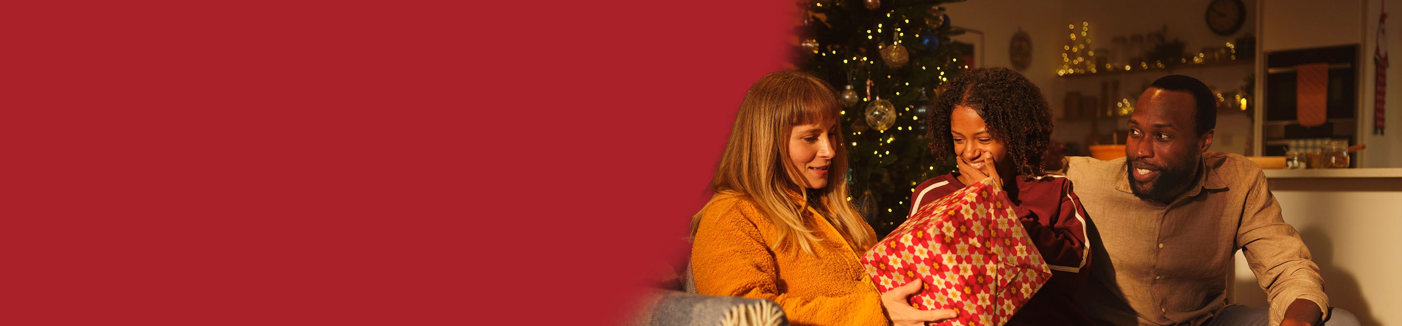 Family sitting by a Christmas tree holding a festive gift bag with holiday decorations in the background
