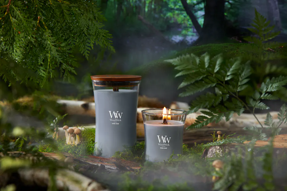 WoodWick Vapour Trails Collection Terra Haze Large Hourglass Candle and Terra Haze Medium Hourglass Candle surrounded by mushrooms, tree branches, moss, and leaves in a forest setting
