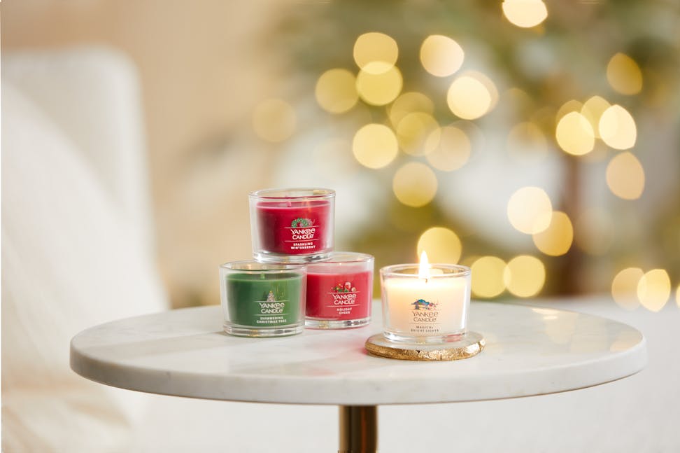 sparkling winterberry yankee candle minis, shimmering christmas tree yankee candle minis, holiday cheer yankee candle minis, and magical bright lights yankee candle minis on a white table with twinkling lights in the background