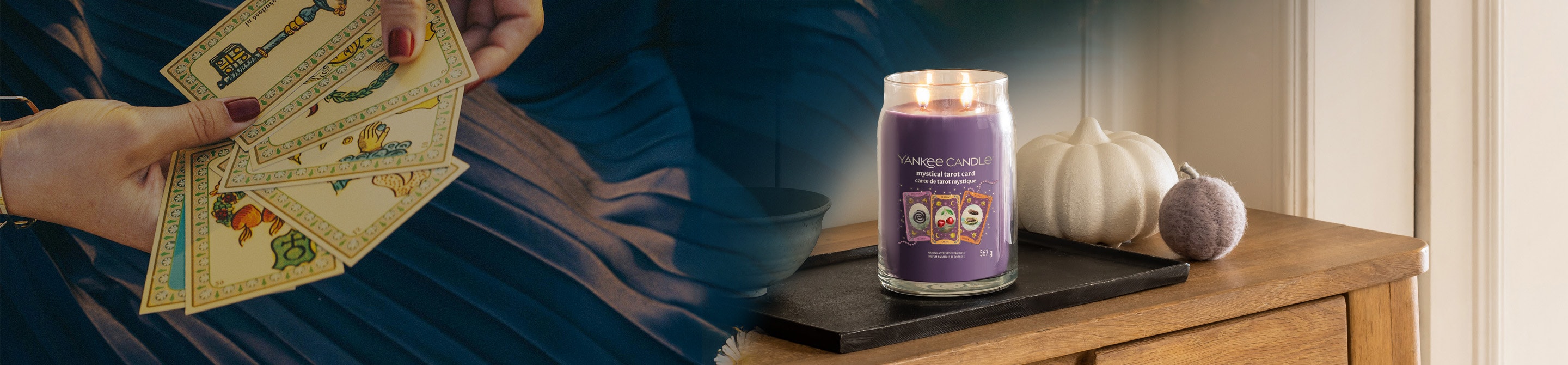 Purple jar candle with three tarot card designs sits on a tray near a white pumpkin on a wooden table
