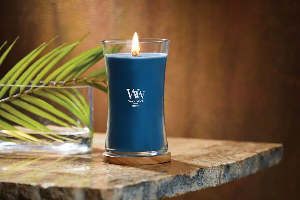 woodwick tempest hourglass candle on wood coaster and stone table with leaf frond in glass bowl
