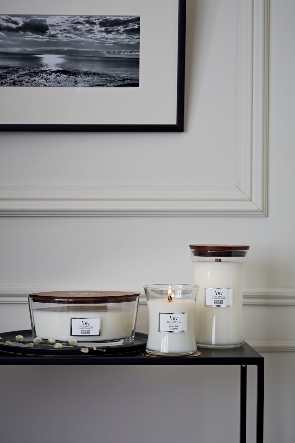 three woodwick white teak candles in various sizes on table