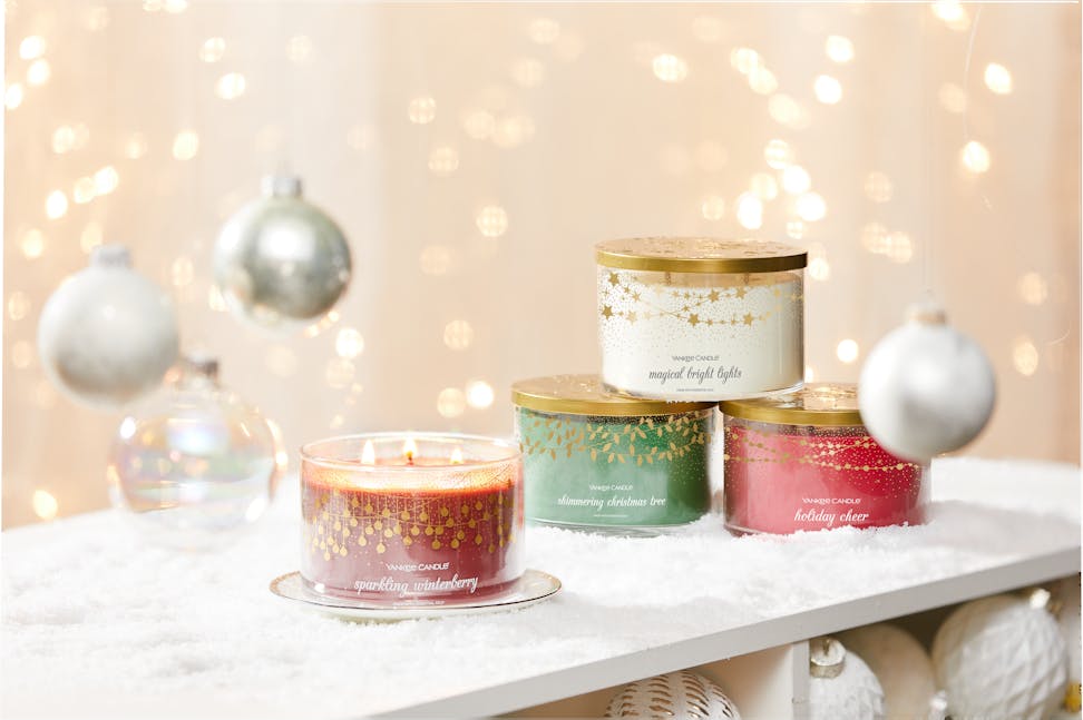four three wick candles on snowy surface with white ornaments and gold sparkles