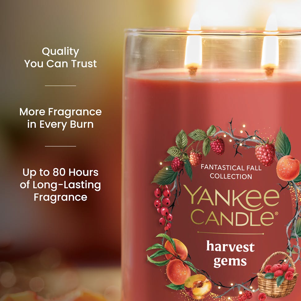Large red fall candle with fruit design, two lit wicks, and text highlighting long-lasting fragrance and quality.