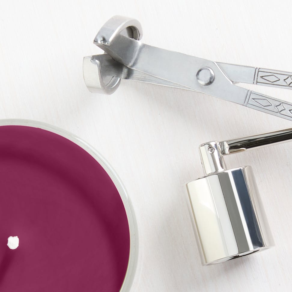 Scented candle with deep burgundy wax and silver wick trimmer, perfect for home decor and relaxation