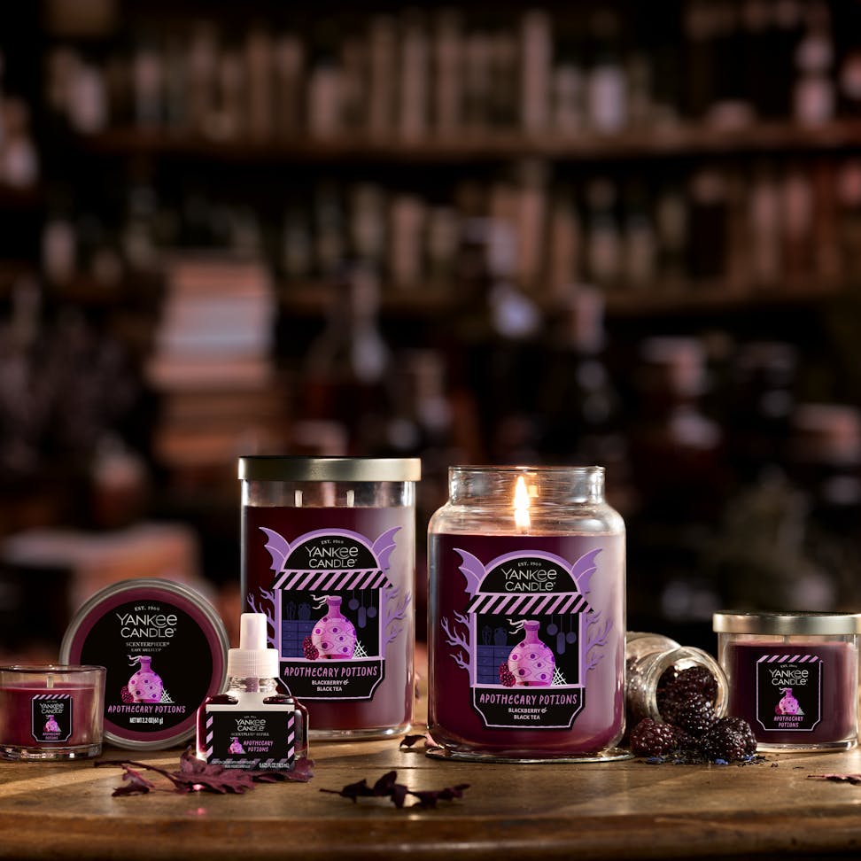Large purple scented candle in glass jar with berries, surrounded by matching home fragrance products on a wooden table