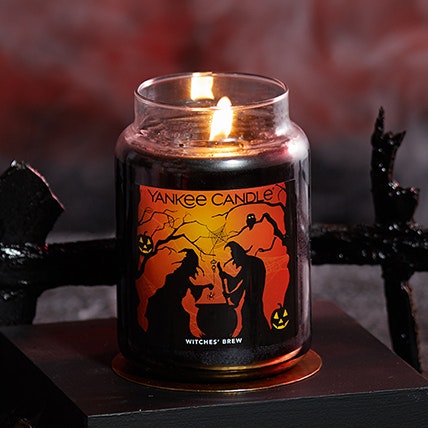 witches' brew original large jar candle with a limited edition label on a black surface with a black fence in the background
