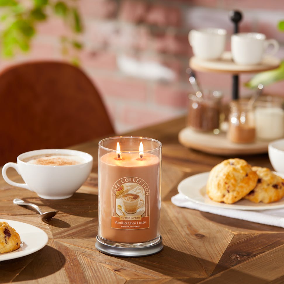 Café Collection Vanilla Chai Latte 'First Sip at Sunrise' Signature Large Tumbler Candle on a wood table with pastries and a latte in a white cup