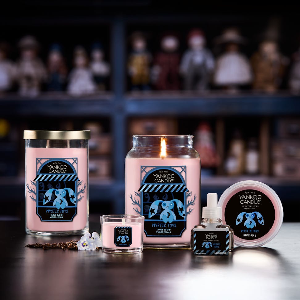 Large pink scented candle with decorative label displayed among matching home fragrance products on a table.