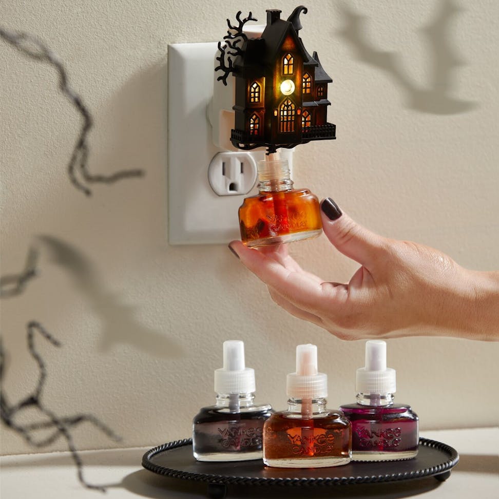 Halloween haunted house plug-in air freshener with glowing light, refill bottles, spooky home decor atmosphere.