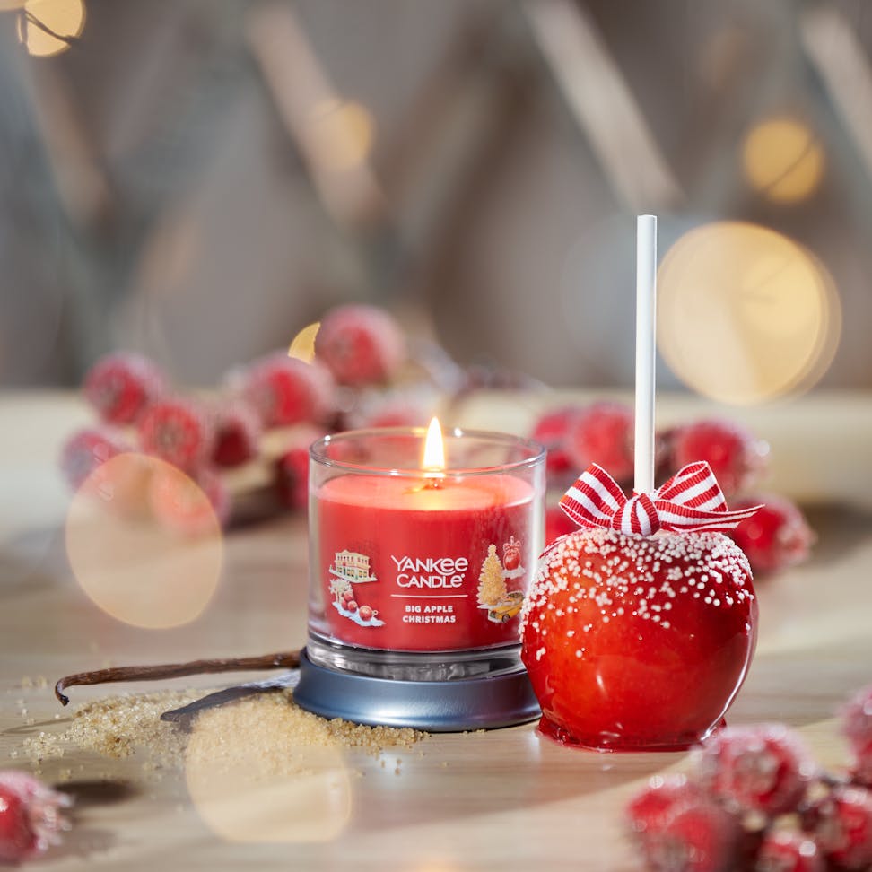 Passport to the Holidays Collection Big Apple Christmas Signature Small Tumbler Candle on a table next to a candy apple