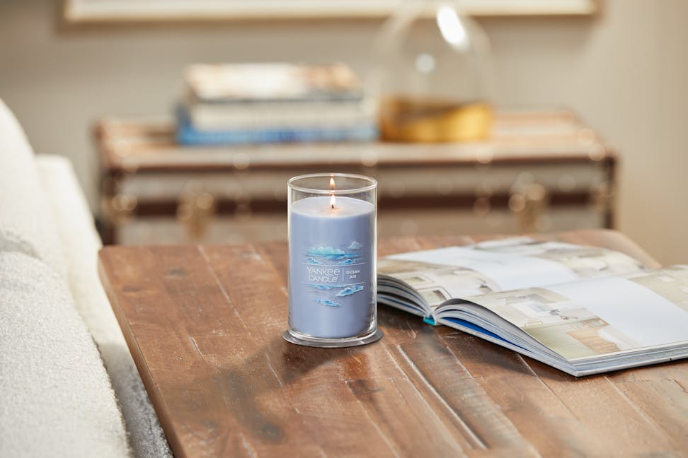 lit ocean air signature medium pillar candle on wooden table next to a book