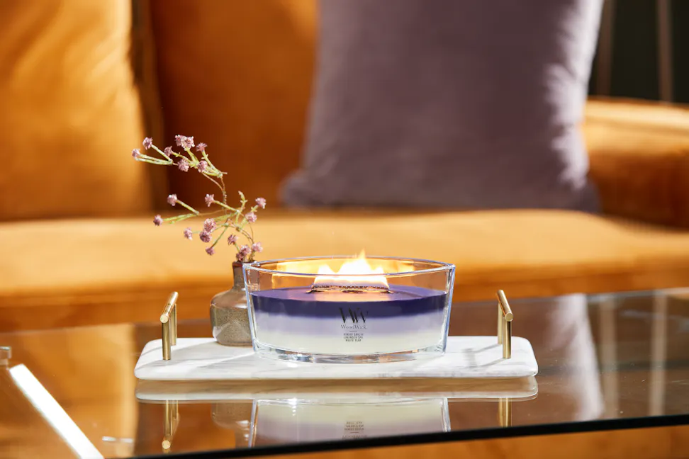 purple trilogy ellipse candle on stone tray with small bottle of flowers on glass coffee table