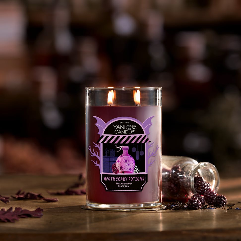 Large purple jar candle with two wicks on a rustic table, next to blackberries and a small glass jar.