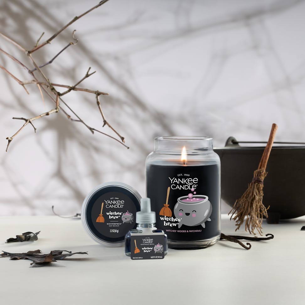 Large black candle with cauldron design, surrounded by autumn decor, broomstick, and fall leaves for Halloween ambiance