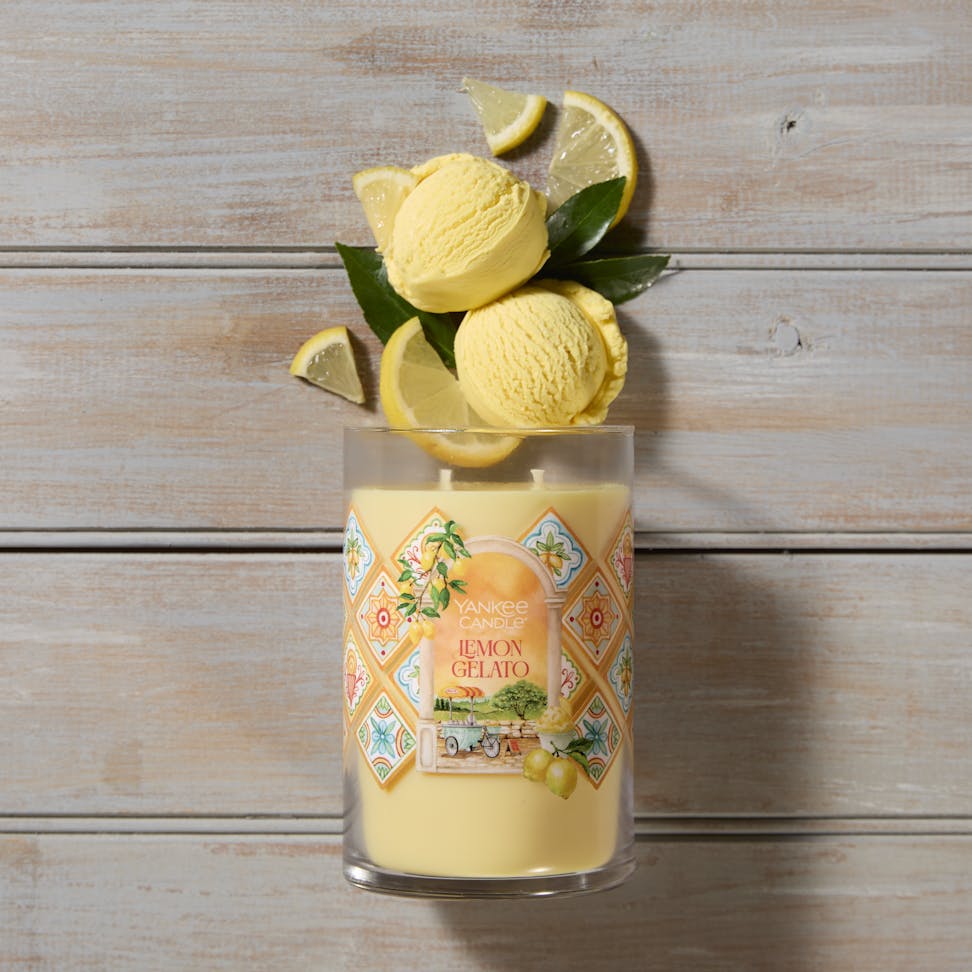 Hello, Italy! Collection Lemon Gelato Signature Large Tumbler Candle laying on a table with scoops of yellow ice cream and lemon slices coming from the top of the candle
