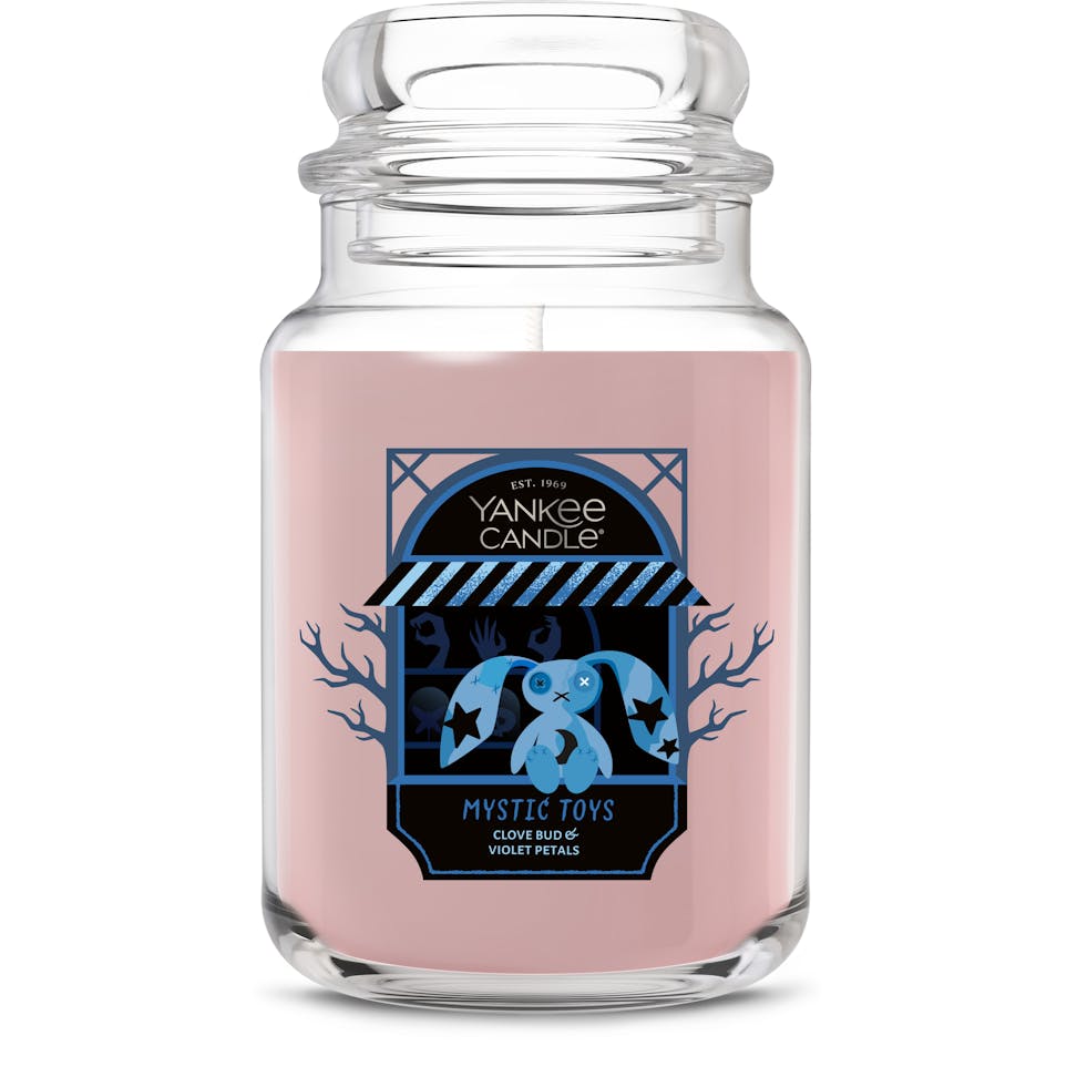 Large glass jar candle with pink wax and a decorative label featuring a blue plush toy and bold black accents