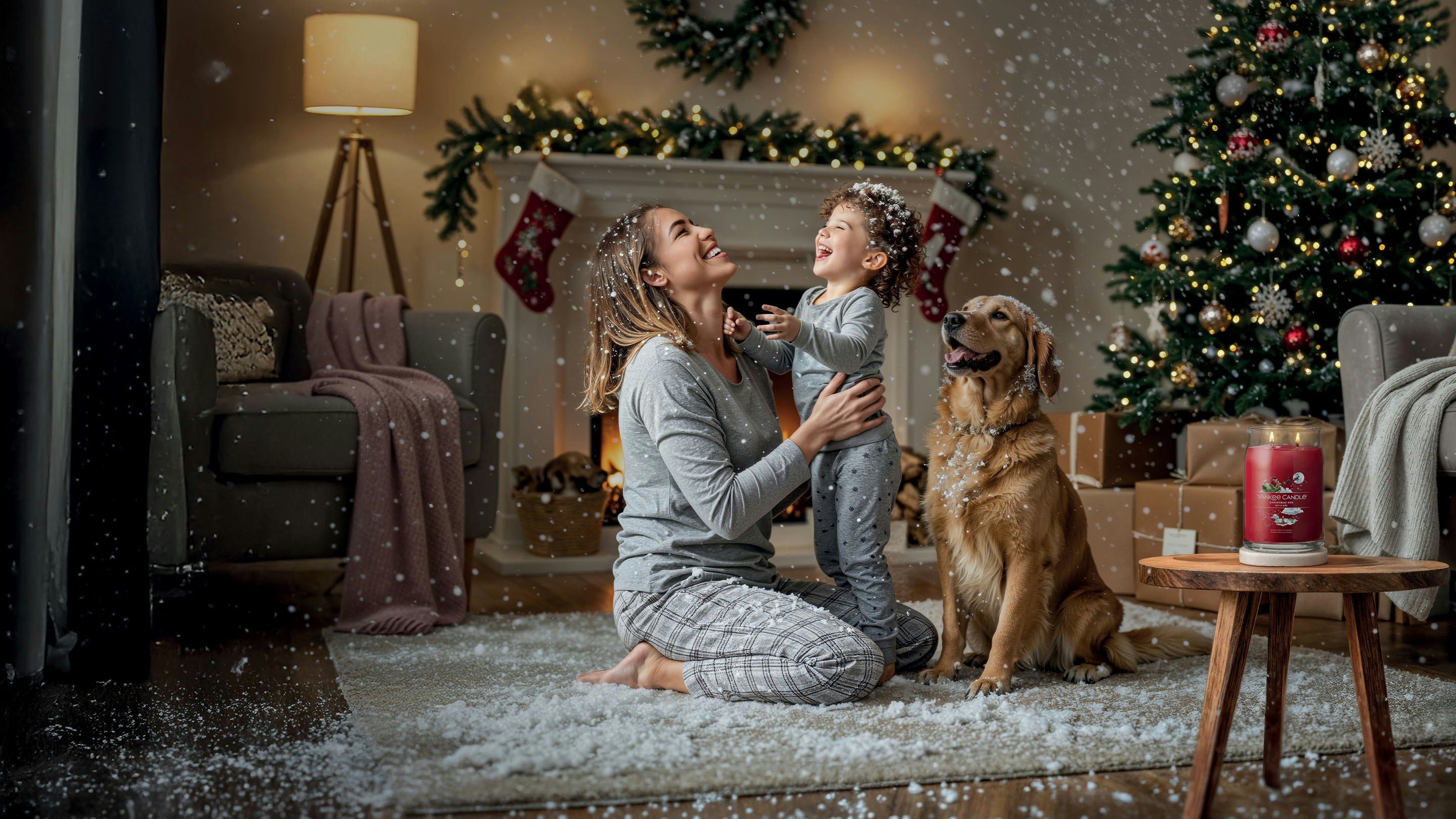 Festive holiday candle on rug near Christmas tree, fireplace, and dog in cozy winter living room with snow effect.