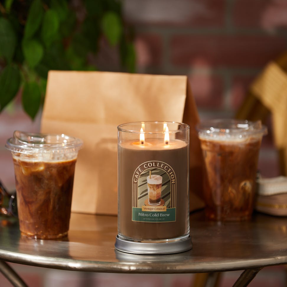 Café Collection Nitro Cold Brew 'Afternoon Pick-Me-Up' Signature Large Tumbler Candle on a small table next to two coffees