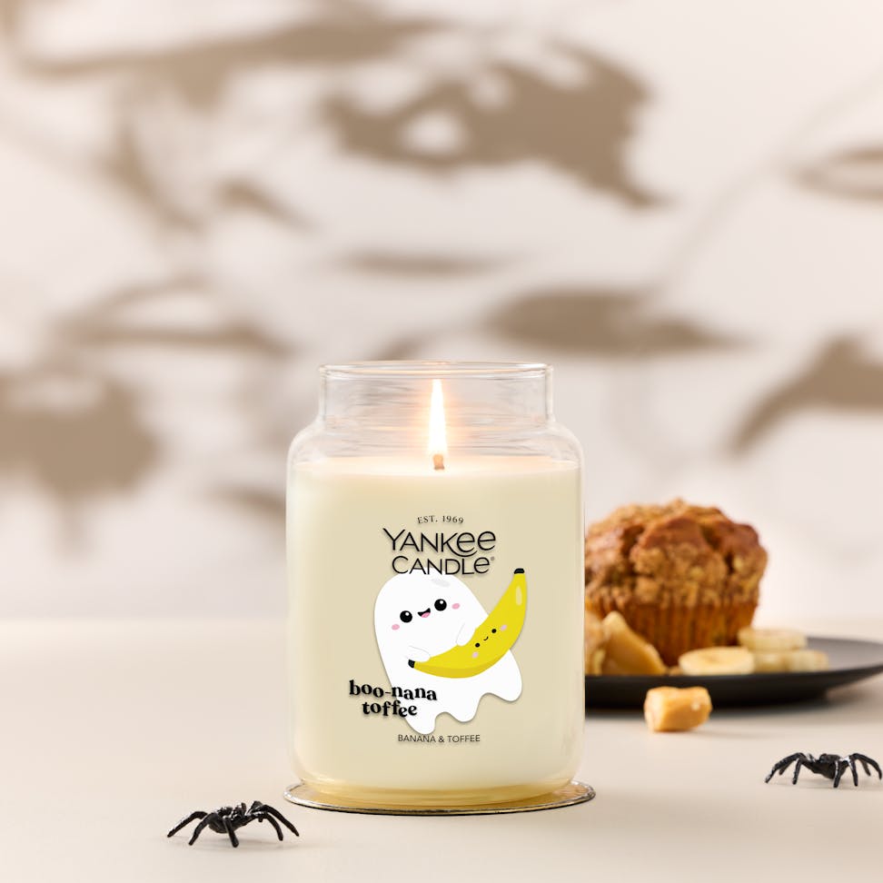 Large Halloween candle with ghost and banana design, lit beside muffin and spiders, boo-nana toffee text visible