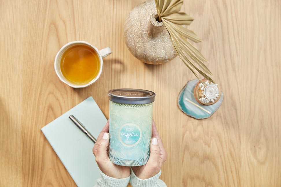 inspire scent of the year signature large tumbler candle being held above wooden table