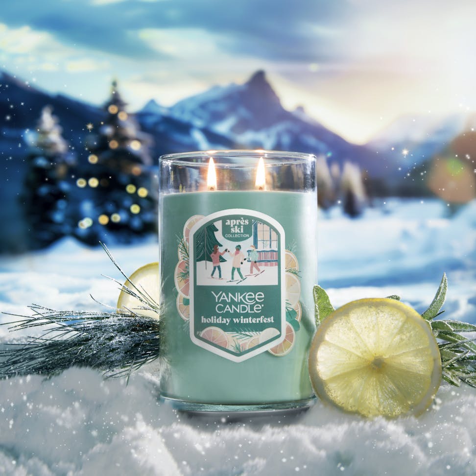 Apres Ski Collection Holiday Winterfest Signature Large Tumbler Candle in snow surrounded by slices of lemon, branches, and mountains