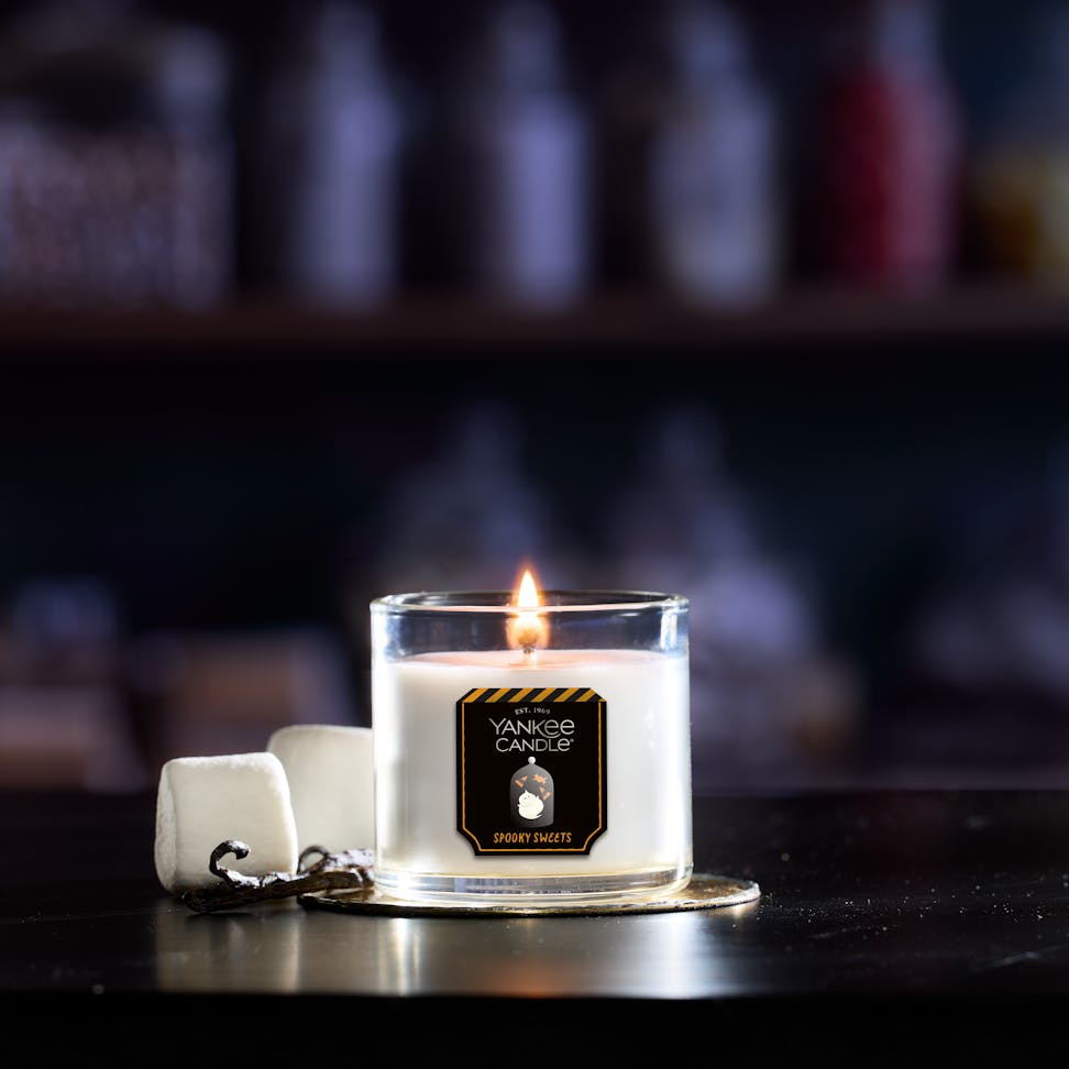 Lit soy wax candle in glass jar with marshmallows beside it, cozy home fragrance decor on table