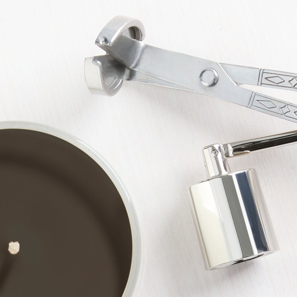 Luxury candle with black wax beside a silver wick trimmer and snuffer for home fragrance care
