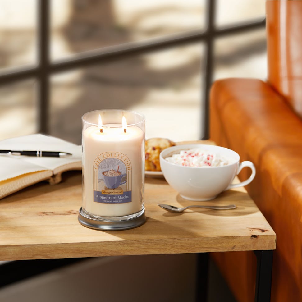 Café Collection Peppermint Mocha 'Grown-Up Snow Day' Signature Large Tumbler Candle on a table next to a latte with whipped cream and sprinkles