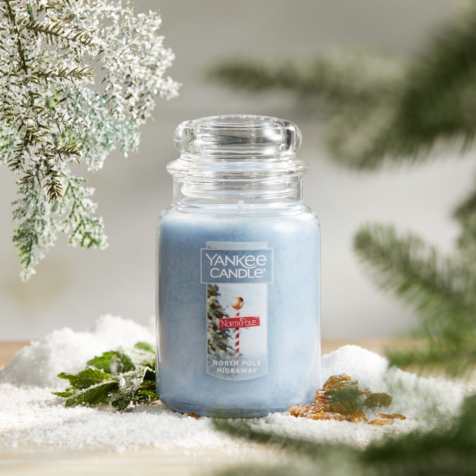 Passport to the Holidays Collection North Pole Hideaway Original Large Jar Candle on a table surrounded by decorative snow