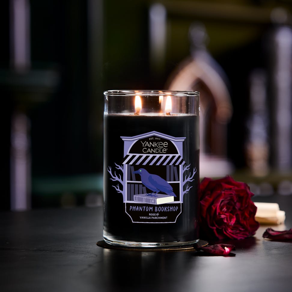 Large black scented candle with two wicks, gothic label, and rose beside, perfect for home decor and ambiance.