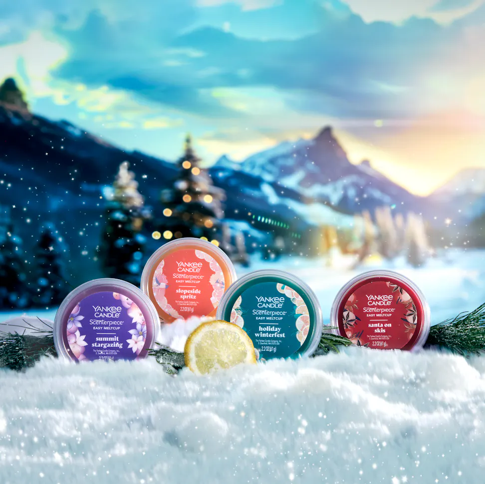 Apres Ski Collection Summit Stargazing Scenterpiece Easy MeltCup, Slopeside Spritz Scenterpiece Easy MeltCup, Holiday Winterfest Scenterpiece Easy MeltCup, and Santa on Skis Scenterpiece Easy MeltCup in snow surrounded by slices of lemon, branches, and mountains