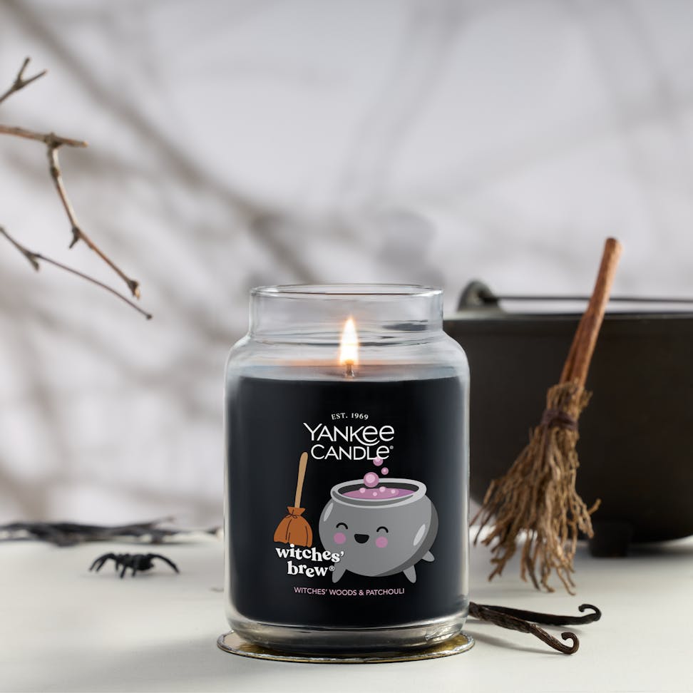 Large black candle in glass jar with cute cauldron design, lit for Halloween home decor and spooky ambiance
