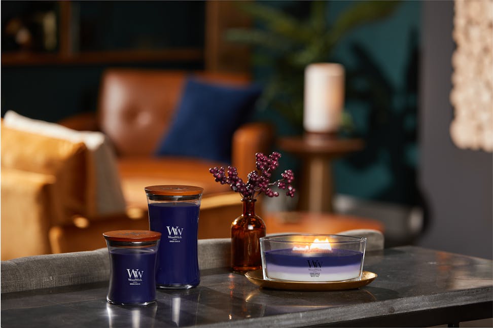 woodwick hinoki dahlia medium hourglass candle, hinoki dahlia large hourglass candle, and evening luxe trilogy ellipse candle with the layered scents of hinoki dahlia, lavender spa, and white teak on a table with a plant