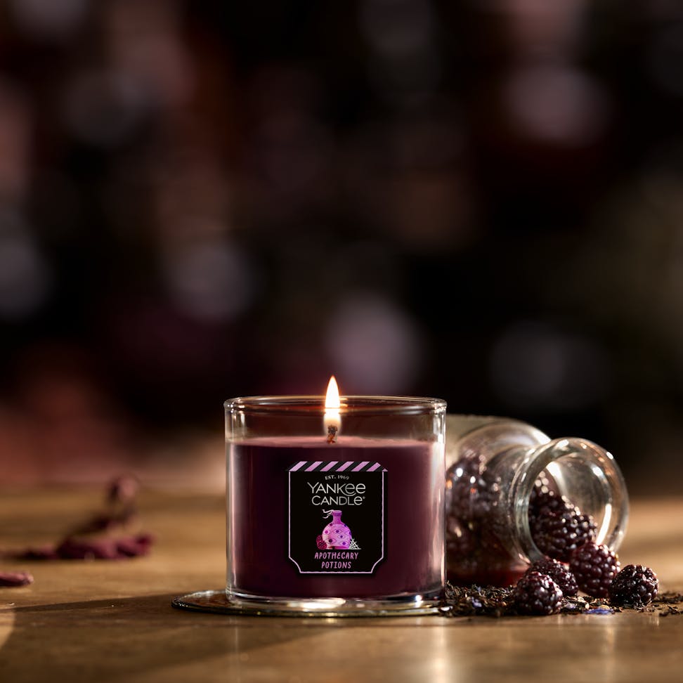 Purple scented candle in glass jar with berries and Apothecary Potions label, cozy home decor ambiance.