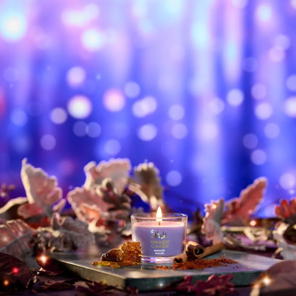 Purple glass candle burning among autumn leaves, cinnamon sticks, and spices with glowing bokeh lights in background