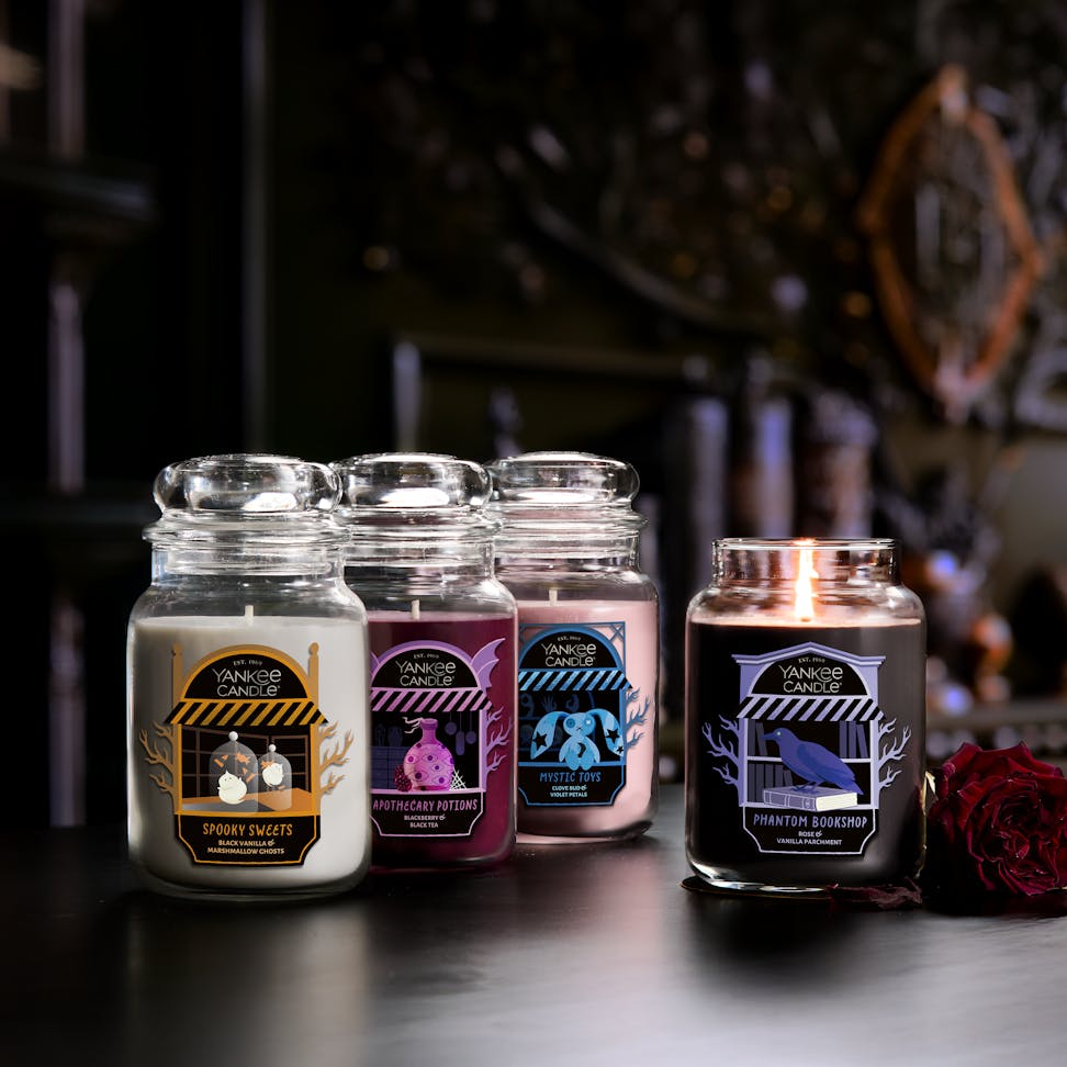 Large glass jar candle with dark label, surrounded by other scented candles, burning for cozy home ambiance.