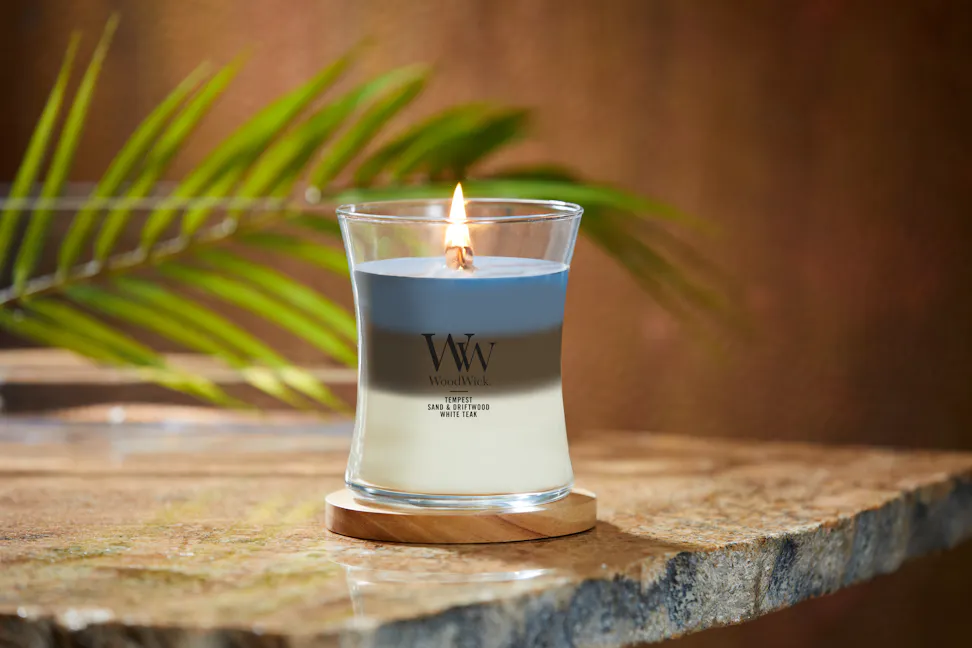 woodwick trilogy hourglass candle on wood coaster and stone table with leaf frond in glass bowl