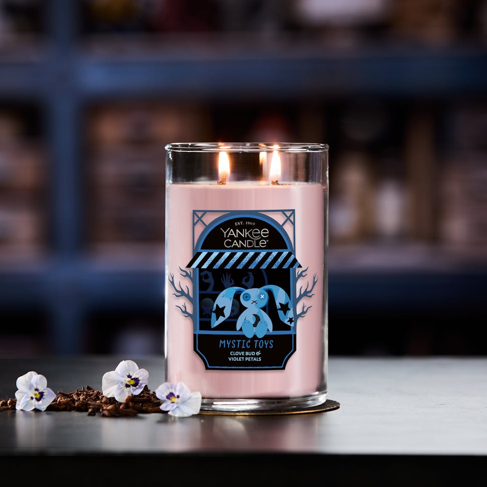 Large pink scented candle with two wicks, decorative label, flowers and spices beside on a table in cozy room